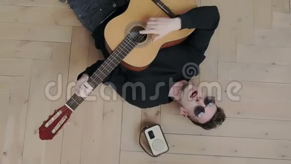 不寻常和真实的千禧一代试图摆脱无聊他躺在木地板上弹声吉他视频的预览图