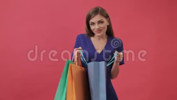美丽的女孩穿着裙子在购物后打开一个带有礼物的包裹工作室粉色背景视频的预览图