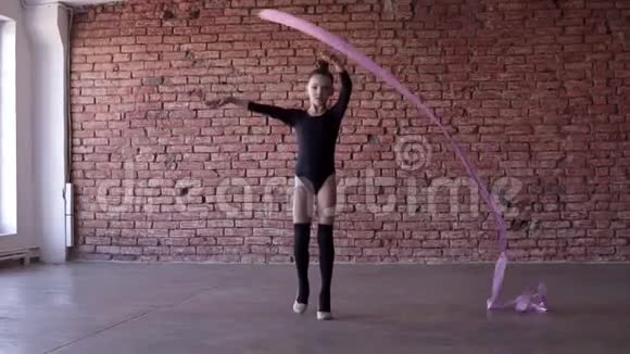 穿黑色紧身衣的小女孩在镜头前用粉色丝带旋转体操的肖像视频的预览图