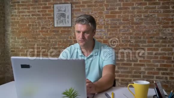 可爱成熟的白种人在工作场所坐着看电脑时玩得很开心跳舞也很开心视频的预览图