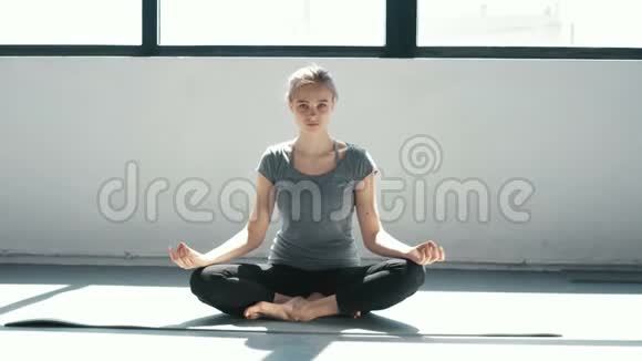年轻漂亮的女人在室内训练期间冥想莲花姿势运动女孩在屋顶上做瑜伽慢动作视频的预览图