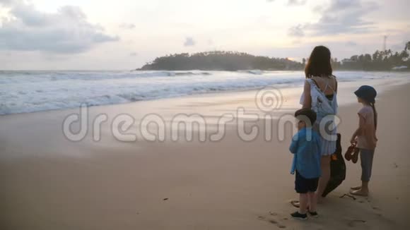 后景快乐的年轻母亲和两个孩子一起在异国情调的热带海滩观看令人难以置信的大气日落视频的预览图