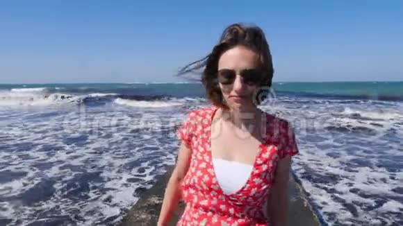 年轻可爱的女人微笑着走在海上码头上强烈的波浪在背景上撞击和飞溅视频的预览图