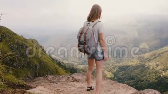 在斯里兰卡史诗般的山景中年轻快乐的女性旅行博主带着背包站着双臂张开视频的预览图