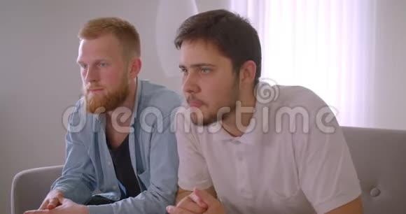 两位长相英俊的白种人成年男子在电视上看体育节目时坐在沙发上感到沮丧的特写镜头视频的预览图