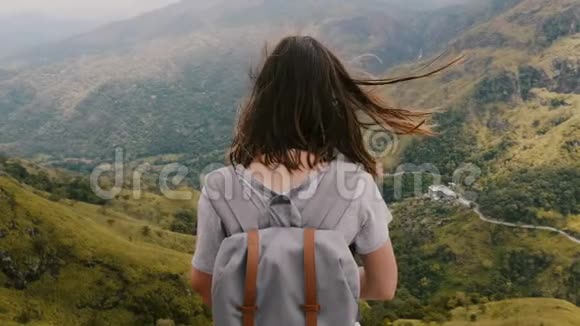 中度后景的快乐旅游女人带着背包和风吹在头发沉思观看史诗般的山景视频的预览图