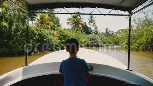 小快乐船长男孩在狩猎之旅船前航行沿着田园诗般的异国丛林河与郁郁葱葱的绿色植物视频的预览图