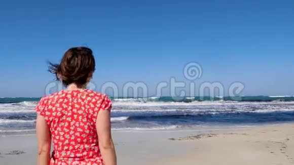 年轻微笑的女人邀请一个男人跟随她走向大海强烈的波浪撞击海滩红色连衣裙和太阳镜视频的预览图