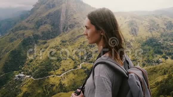 特写镜头年轻的旅游妇女带着背包和相机在她的头发上享受风在惊人的山景视频的预览图