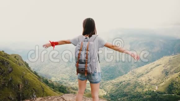 在斯里兰卡史诗般的山景中带着背包的年轻快乐旅游妇女张开双臂向空中望去视频的预览图