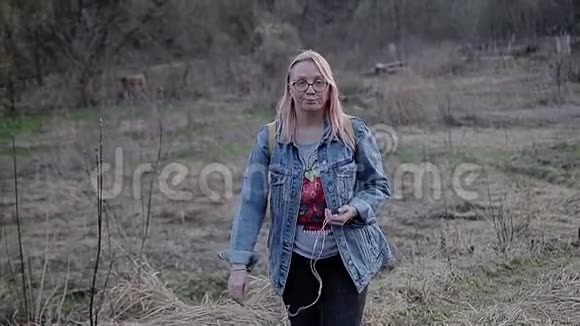 女孩走在荒原上微笑着看着镜头女孩戴着白色眼镜蓝色牛仔夹克和一件视频的预览图