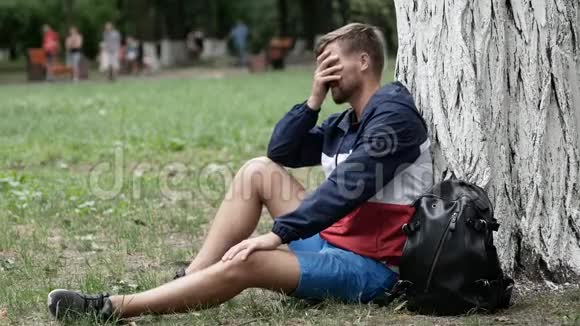 失望沮丧的男人坐在树下思考生活用手遮住他的脸阴性视频的预览图