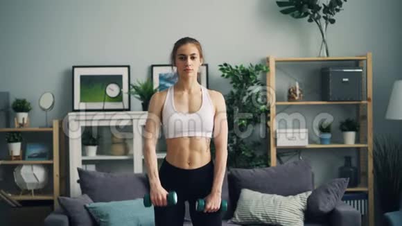 穿运动服的强壮的年轻女子在公寓里用哑铃做运动视频的预览图