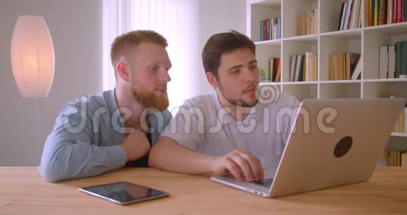 两位成年白种人商人使用笔记本电脑并在室内进行讨论的特写照片视频的预览图