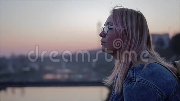 日落时坐在河堤上的女孩的美丽计划在年轻女孩的白色镜头上视频的预览图