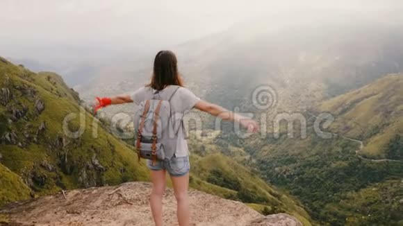 镜头放在年轻快乐的旅游妇女的身后她背着背包在斯里兰卡的史诗般的群山中举起双臂向空中望去视频的预览图