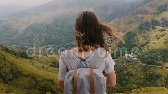 近距离后景兴奋的年轻旅游妇女背包张开双臂观看斯里兰卡史诗般的山景视频的预览图