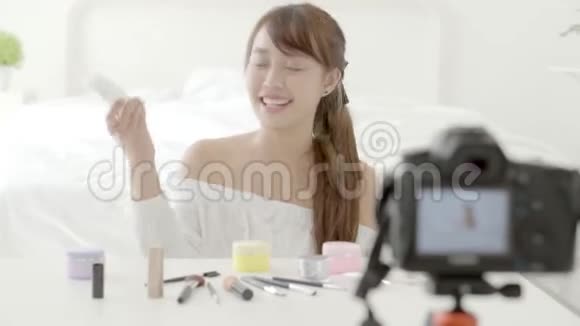 美丽的亚洲年轻女性在家里用视频和vlog显示化妆霜或化妆水视频的预览图