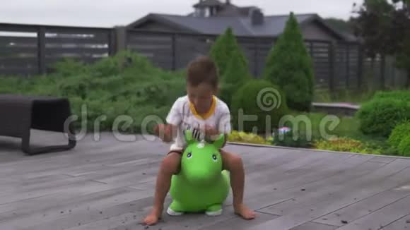 在绿色的花园里骑着绿色的玩具马的小男孩儿子跳跃家庭价值观温暖的颜色夏天的场景视频的预览图