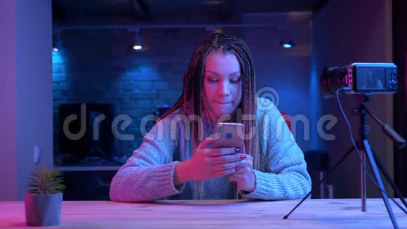 一位年轻有魅力的女性博客写手在手机上发着可怕的短信用霓虹灯直播视频的预览图