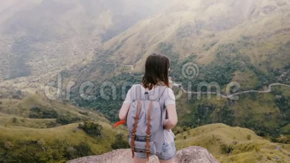 在斯里兰卡令人叹为观止的山景中背高角度观看快乐的旅游妇女与背包触摸头发视频的预览图