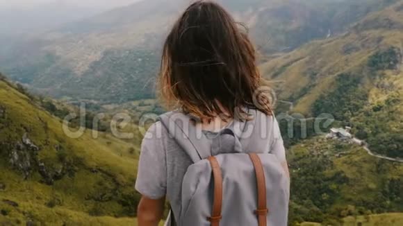 中等后景拍摄年轻快乐的女人带着背包和飞扬的头发徒步旅行观看斯里兰卡令人难以置信的山脉视频的预览图