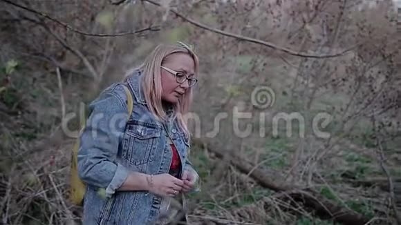 一个穿蓝色牛仔裤的女孩弯着头从树枝下经过美丽的电影框架回放缓慢视频的预览图