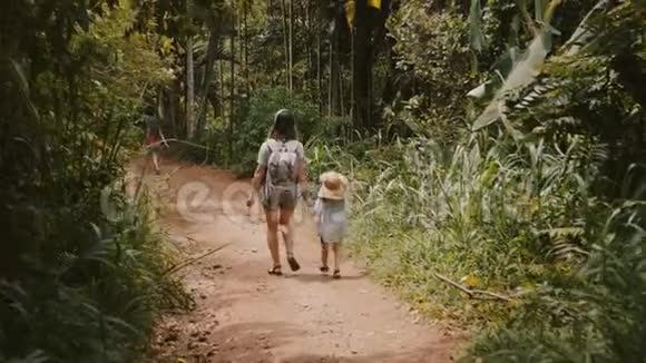 后景幸福的小妈妈和小孩子一起戴着大草帽走在陡峭的森林道路上慢动作视频的预览图