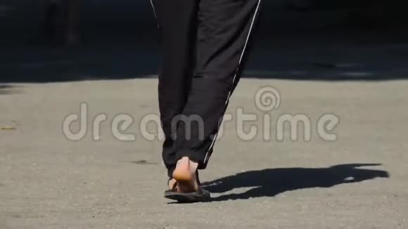 一个男人穿着黑色运动裤和拖鞋走在街上视频的预览图