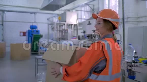 工厂里的女强人幸福的女强人戴着安全帽穿着工作服穿过工厂里的大箱子视频的预览图
