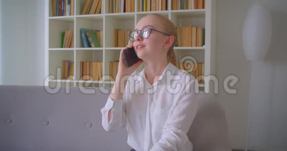 年轻漂亮的白种人金发女生戴眼镜坐在沙发上打电话的特写照片视频的预览图