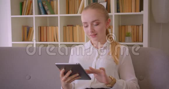 年轻漂亮的白种人金发女学生的特写镜头她用平板电脑看着坐在上面微笑的镜头视频的预览图