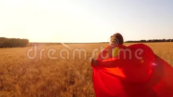 孩子梦想飞翔女孩穿着红色雨衣扮演超级英雄在蓝天上沿着黄色的田野奔跑快乐的童年视频的预览图