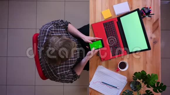 一位年轻的高加索商人在笔记本电脑前用绿色屏幕的手机拍摄特写镜头里面放着咖啡视频的预览图