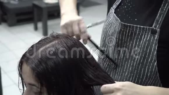 剪发的特写女理发师的梳子和剪刀剪湿了头发的东方女孩坐在理发店里视频的预览图