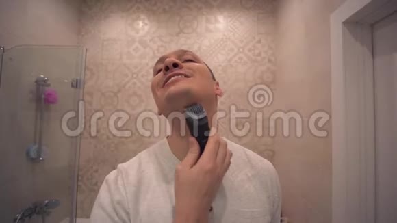 成熟的英俊男子在浴室的镜子前用电动剃须刀刮脸胡茬视频的预览图