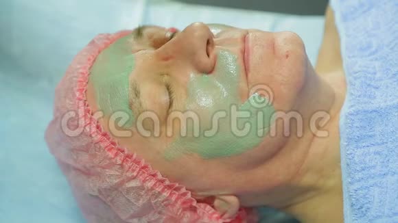 戴手套的女美容师用一个带刷子的治疗粘土面具对着男人的脸视频的预览图