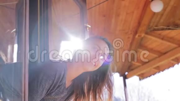阳光明媚的一天年轻的微笑的女人从山上一座乡间小屋的窗外望去视频的预览图