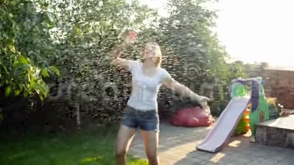 日落时分穿着白色t恤在温暖的夏雨下跳舞和跳跃的快乐微笑年轻女子的慢镜头视频的预览图