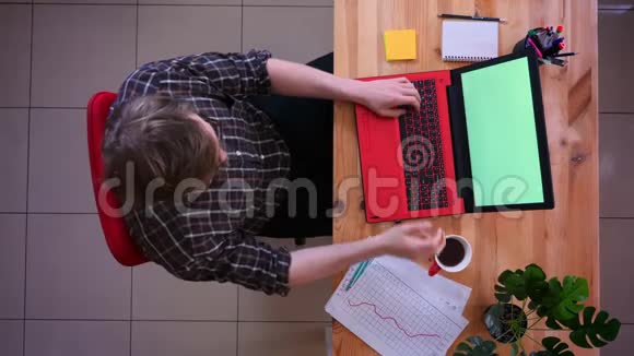 一位年轻的白种人商人用绿色屏幕在笔记本电脑上工作并在里面喝咖啡这是他的特写镜头视频的预览图