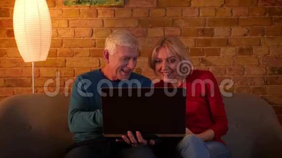 在一间舒适的公寓里坐在沙发上的高级幸福夫妇在笔记本电脑上使用社交媒体的特写镜头视频的预览图