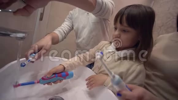 晨间卫生年轻的妈妈和爸爸在镜子前用牙刷教孩子刷牙视频的预览图