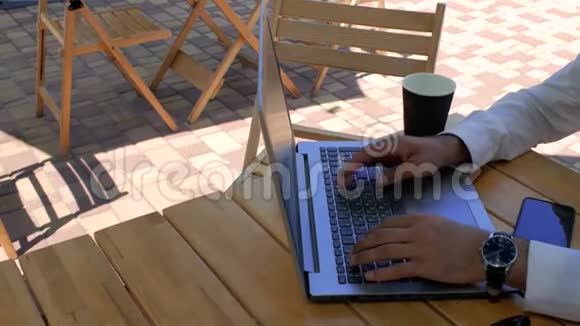 一个穿着白色衬衫的男人坐在街头咖啡馆的桌子旁在笔记本电脑键盘上打字从上面看4k4k视频视频的预览图