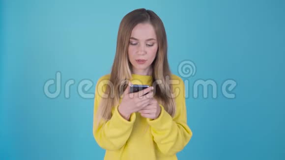 快乐满意的女孩看着手机和欢呼孤立在蓝色背景4K视频的预览图
