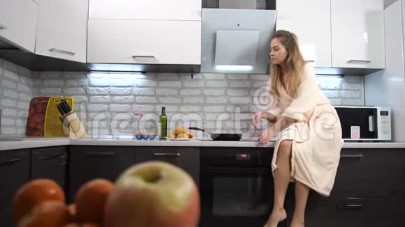 一个苗条的女孩坐在厨房的桌面上急切地吃着一个面包4K慢慢视频的预览图