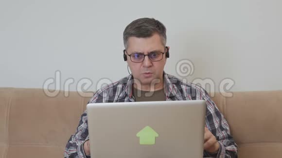 坐在沙发上拿着笔记本电脑的中年男人表情鬼脸地看着屏幕视频的预览图