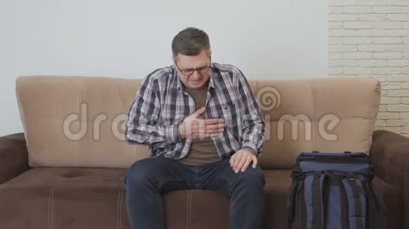 一个中年男子坐在沙发上手握在心脏区域感觉到剧烈的疼痛一个男人呼唤视频的预览图