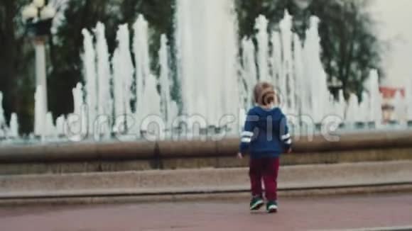 一个小男孩在喷泉前散步与父母同行父母照料视频的预览图