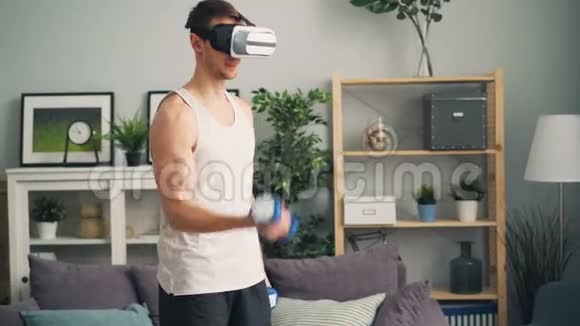 一位戴着时髦虚拟现实眼镜的年轻人正在家里用哑铃锻炼身体视频的预览图