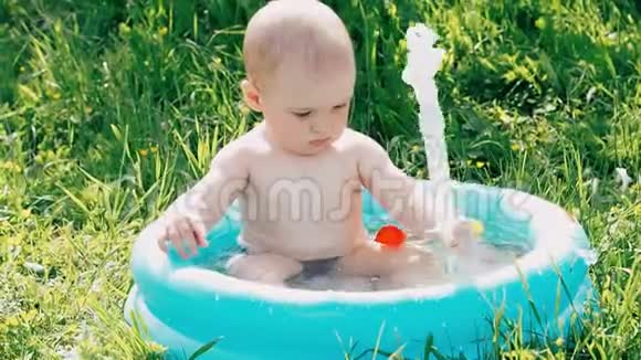 小男孩在充气游泳池里游泳夏天在绿色草地上玩耍视频的预览图